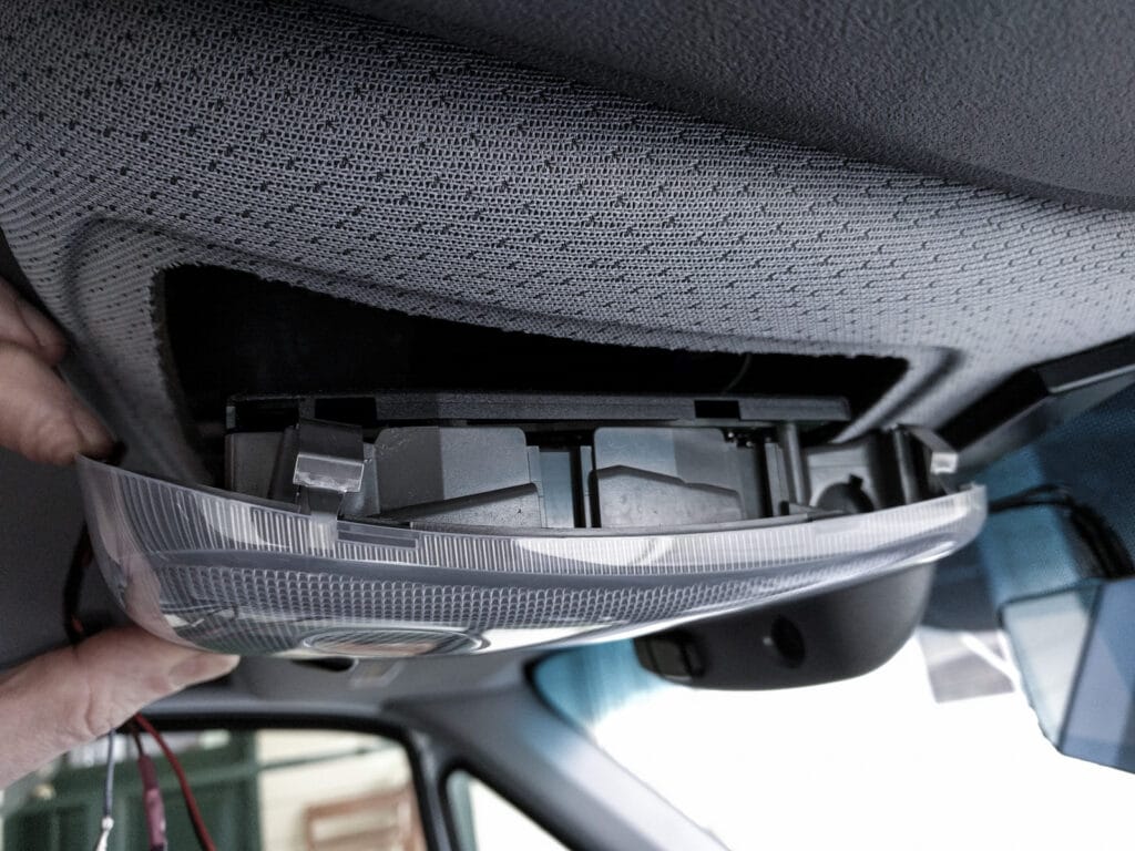 The passenger side of the courtesy light cluster has two metal spring clips. The driver's side has two plastic tabs. Push the spring clips in and hinge the unit down to remove it.